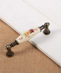 Vintage Ceramic Drawer Handles In Antique Bronze With Elegant Flower Pattern resting on wooden surface