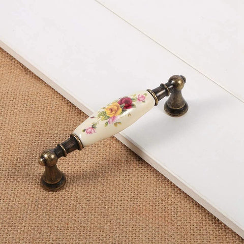 Vintage Ceramic Drawer Handles In Antique Bronze With Elegant Flower Pattern resting on wooden surface