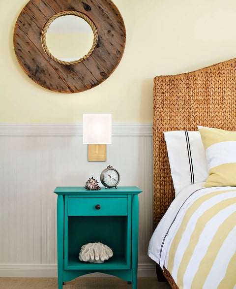 Gold Mid Century Wall Sconces Set Of 2 With White Linen Shade next to bed with rattan headboard in cozy hotel vibe setting