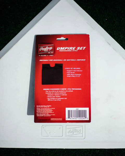 Back packaging of Umpire Gear Kit With 4-Dial Indicator, Plate Brush, And Pro-Style Cloth Bag, placed on home plate.