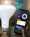 Dimmable WiFi Smart LED BR30 Flood Bulb next to smartphone app for brightness control, featuring E26 base for indoor use.