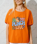 Woman in orange shirt with 'In My Punch Era' graphic, showcasing color text and cartoon bears with floral accents and sunglasses.