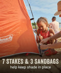 Lightweight Beach Shade Tent with pre attached poles, side view, sand setup, showing 7 stakes, 3 sandbags, family nearby