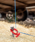 Close-up of Beefy Aluminum Ground Anchor holding blue wire, used for tents and outdoor gear, with spiral blade grip and red holder.