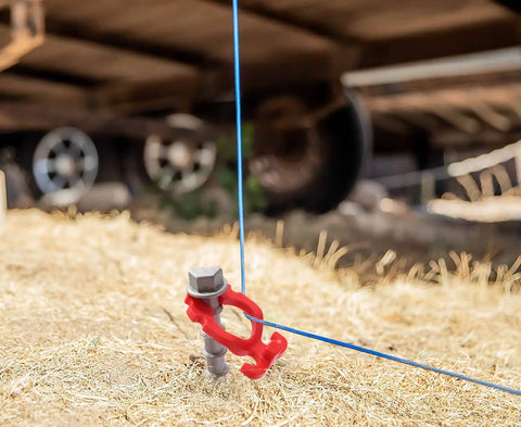 Close-up of Beefy Aluminum Ground Anchor holding blue wire, used for tents and outdoor gear, with spiral blade grip and red holder.