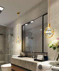 Dope Modern Crystal Pendant Light In Gold Brushed Brass Finish with 4.33 Inch K9 Crystal, installed in a bathroom setting.