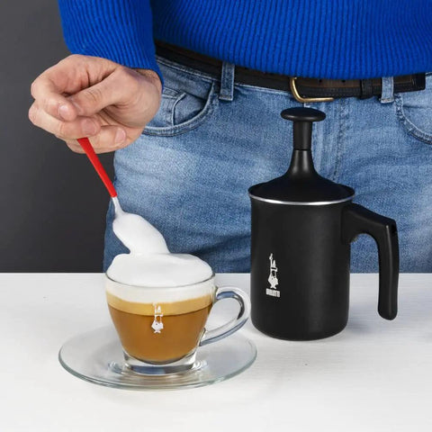 Tutto Crema Milk Frother Black Barista Grade, 1L Capacity with double mesh, next to a frothy coffee cup on a table.