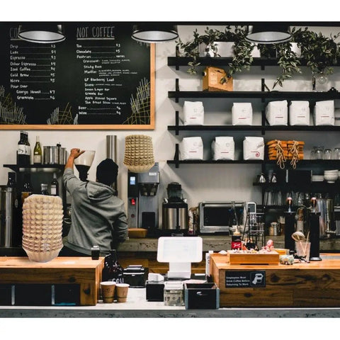 Hella Durable Unbleached Brown Biodegradable Coffee Filters Fit 10 To 15 Cup Baskets in a cafe setup with coffee equipment.