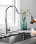 High Arc Kitchen Faucet With Pull Down Sprayer Single Handle Sink Faucet In Brushed Nickel next to a hand filling glass with water