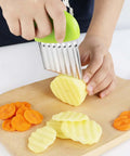 Two stainless steel crinkle cutters with green handles, slicing potatoes and carrots into wavy chips on a board.