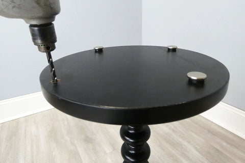 Installing Beat The Wobble Instantly 1 1/4 Inch Round Floor Protectors with a drill on a black table surface.