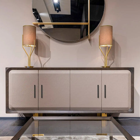 Modern sideboard with matte black square cabinet handles, flanked by gold lamps, below a large round mirror.