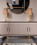 Modern cabinet with four doors and black handles, topped with gold lamps, under round mirror in home interior.