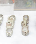 Four machined metal components displayed in a showcase, used for industrial applications such as automotive or machinery.