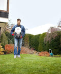 Man using 9 Kg Capacity Manual Spreader With Adjustable Strap And Crank, Red, A Yard Work Must-Have For Even Spreads in a garden