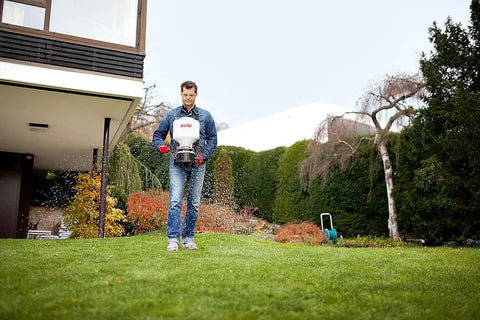 Man using 9 Kg Capacity Manual Spreader With Adjustable Strap And Crank, Red, A Yard Work Must-Have For Even Spreads in a garden