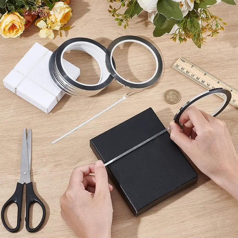 Person applying Premium Metallic Mirror Trim Tape Heavy Duty Pet Self Adhesive Roll to a black gift box alongside scissors.