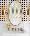 Gold Brass Wall Sconces Set Of Two Modern Two Light Vanity Lights flank oval mirror in bathroom with black and white wall tiles.