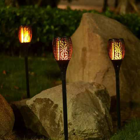 Solar Torch Light With Flickering Flame Dancing Flame Outdoor Lanterns Waterproof Garden Stake Lights in garden setting at night.