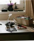 Helping Hands Soldering Tool With LED Magnifying Lamp And Adjustable Arms on a desk next to a metal toolbox and soldering iron.