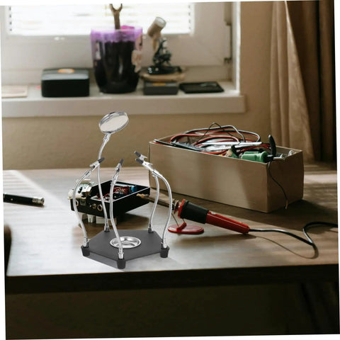 Helping Hands Soldering Tool With LED Magnifying Lamp And Adjustable Arms on a desk next to a metal toolbox and soldering iron.