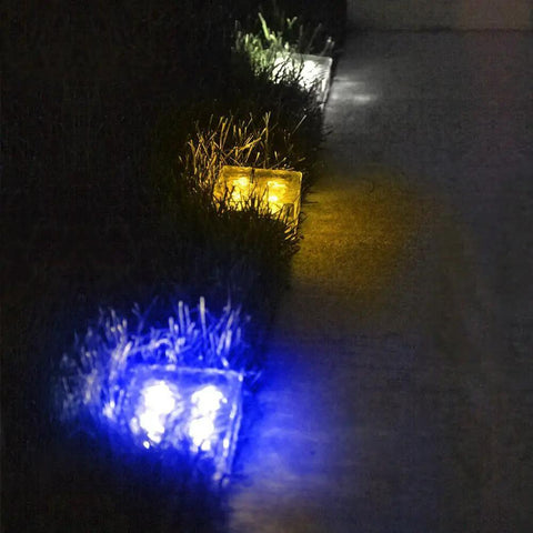 Ice Cube Solar Glass Brick Path Lights 4 Pack For Garden And Yard, glowing in blue and yellow in a nighttime garden setting.