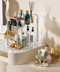 Clear 3 Tier Acrylic Rolling Storage Cart With Four Extension Poles For Tall Items And Bottles Laundry Room Bathroom Office Or Living Room Organization Mobile Multifunction Shelving Unit on a vanity holding various beauty products.