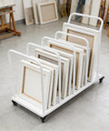 Heavy Duty Rolling Carton Stand With Adjustable Divider Slots And Smooth Lockable Wheels Solid Iron Flatbed Storage Cart Built For Warehouse Grind Or Workday Hustle White with stacked picture frames