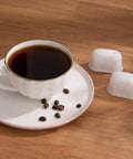 Cup of coffee with coffee beans next to two BWF100 replacement filters, fits Breville espresso machines, on a wooden table