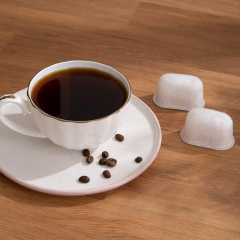 Cup of coffee with coffee beans next to two BWF100 replacement filters, fits Breville espresso machines, on a wooden table