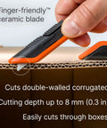 Slice box cutter with orange and black handle and ceramic blade cutting cardboard.