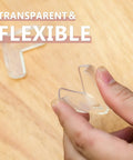 Transparent corner protector being held, part of 12 Pack Transparent Corner Protectors For Tables And Desks Soft Pvc Furniture Edge Bumpers.