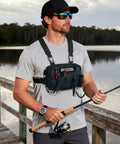 Man fishing wearing a water resistant outdoor chest bag for men with lightweight tactical design, black camo color, on a dock.