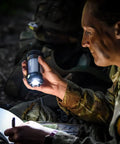 Person using Siege X Rechargeable Lantern Flashlight 360 Degree Light at night, illuminating notebook and face, wearing military uniform.