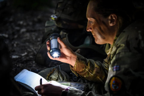 Person using Siege X Rechargeable Lantern Flashlight 360 Degree Light at night, illuminating notebook and face, wearing military uniform.