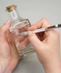 Person using Heavy Duty Tungsten Carbide Scriber Engraving Pen on a glass bottle, marking for crafting projects.