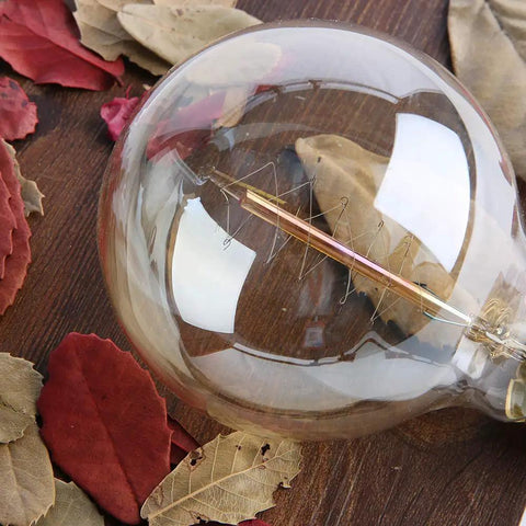 Vintage Edison Style G25 Globe Bulbs 60W Amber Glass Dimmable Round Bulbs 2100K Warm White E26 Base Old School Incandescent Mood Lighting 4 Pack Great For Dinners, Bars, And Ambient Home Decor on wooden table with autumn leaves