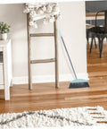 Grime Crushing Heavy Duty Broom With 34 Inch Long Handle For Sweeping Concrete Driveway Garage Patio And Indoor Floors No Sweat Household Cleaner With Convenient Storage Hook leaning against a wooden ladder.