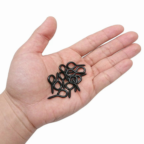 Hand holding 100 Pack 1 Inch Metal Screw Eyes Hooks Self Tapping Eye Rings For Indoor Outdoor Hanging Lifting And Securing Cables.