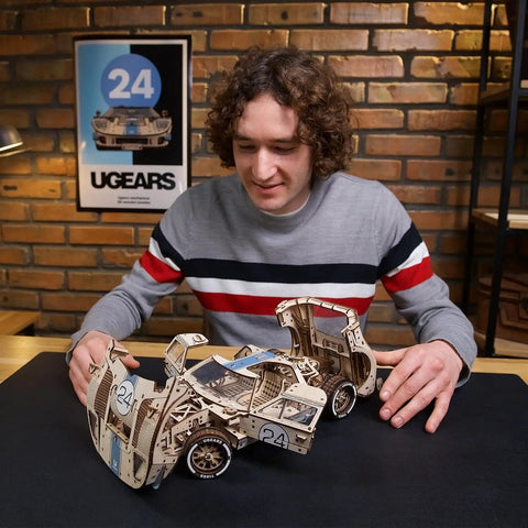 Endurance Racer DIY Model Car Kit 3D Puzzle, Dope Mechanical Wooden Sports Car For Adults To Build One Twelfth Scale, Vintage 1960s Inspired Hobbyist Kit With Real Working Gears, Movable Parts, And Easy To Follow Instructions For First Time Builders. man assembling 1:12 wooden race car model
