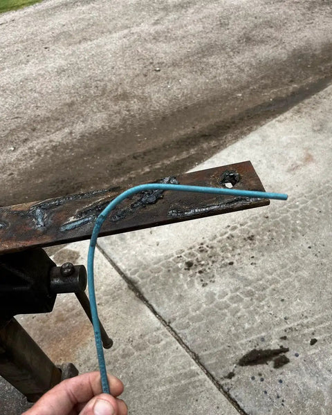 Hand holding a Tartan AAA Welding Electrode One Eighth Inch Diameter For Mild Steel Repairs against a welded metal surface.