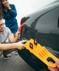 Professional Grade Paintless Dent Removal Kit Featuring Sturdy Pullers And Strong Glue Tabs To Knock Out Dinged Up Bumpers Fenders And Hoods Restore Your Banged Up Ride Clean Now in use on a black car.