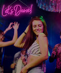 Young adults dancing under Lets Dance Neon Sign Pink LED Word Light for Weddings and Parties, vibrant party atmosphere.