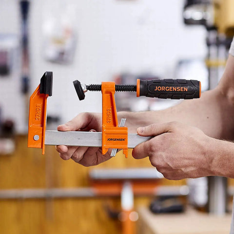 Heavy Duty 6 Inch Steel Bar Clamp for Woodworking and DIY Projects, Orange, Sure Grip Construction, Reaches Up To 3 Inches From Edge To Screw Center, Maximum Opening 6 Inches, Built For Hard Use By Hobbyists And Pros. Orange steel bar clamp holding wood in workshop