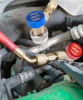 Close-up of brass R134a refrigerant service adapters with blue low-pressure and red high-pressure caps on engine hoses