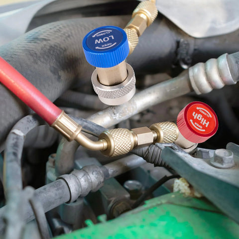 Close-up of brass R134a refrigerant service adapters with blue low-pressure and red high-pressure caps on engine hoses
