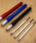 Three color-coded aluminum lathe tool handles in red, blue, and black with four silver carbide bits on a wooden surface