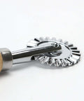 Close-up of a zinc alloy crinkle pizza cutter wheel with a long wooden handle.