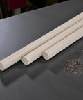 Beige PEEK Plastic Round Rod One Quarter Inch by 24 Inches Three Pack for engineering projects and fabrication on a workshop table.