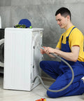 Man repairing washing machine, wearing blue overalls, handling hose